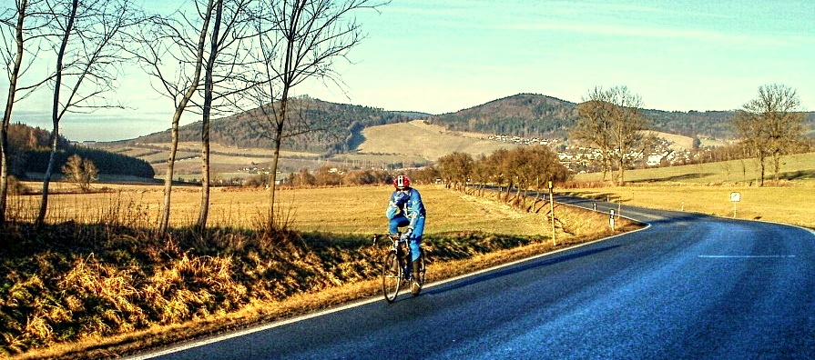 Cyklista jede opačným směrem než já, dole Jsou Prapořiště, pod lesem Starec.